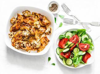 Baked chicken breast with cauliflower cabbage and fresh tomatoes, cucumbers, greens salad on a light background, top view