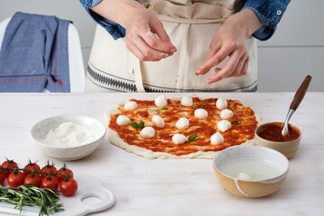 Woman adding basilic on pizza. Woman doing homemade pizza.