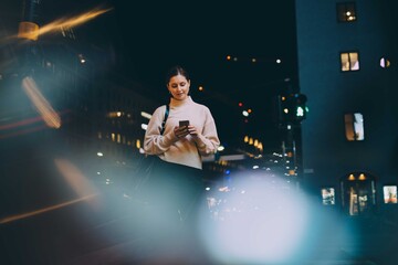 Young woman texting through smart phone while standing in city at night