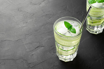 Detox cold drink with sliced cucumber and mint leaves in glasses. Dark slate table. Copy space.