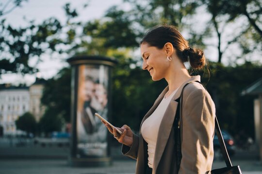 Smiling woman using social media while standing in city