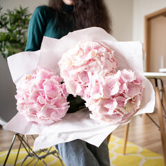 Young woman holds light tender pink hydrangea bouquet, closeup photo in home interior