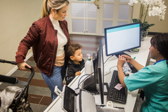 High angle view of pediatrician giving stickers to boy while mother standing with baby stroller in hospital