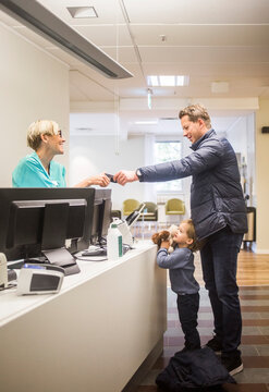 Side view of mature man giving id card to doctor while son standing by reception in hospital