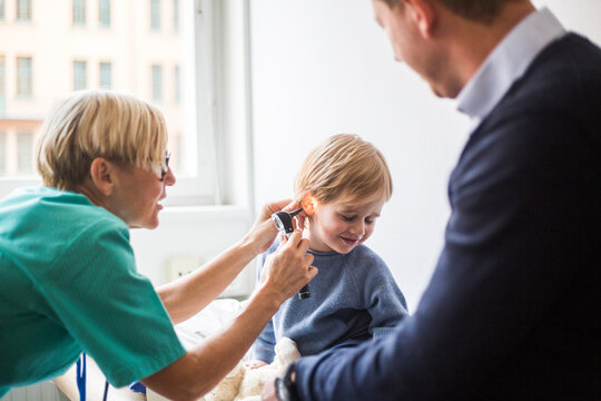Female doctor examining boy's ear with otoscope while sitting by father in hospital