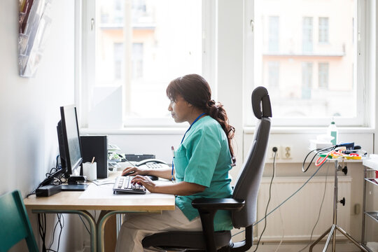 Side view of mature female doctor working over computer while sitting in clinic
