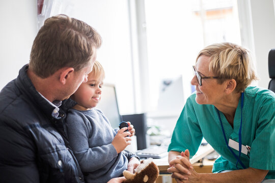 Smiling mature doctor talking to boy with father in clinic