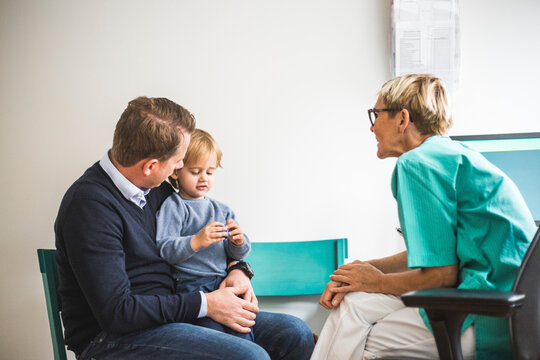Side view of mature female doctor talking to boy with father in clinic