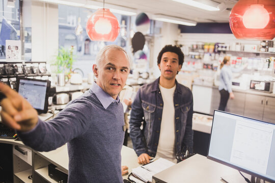 Male owner pointing while customer standing in background at electronics store