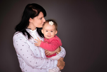 Portrait of cute baby girl and her young mother on grey background.