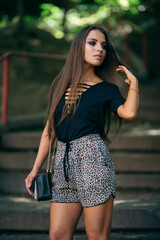 Fototapeta premium A beautiful and charming girl in full height looks at the storna, holds a bag and hair. Expressive brown eyes, black jacket. Back background aside. half-length portrait