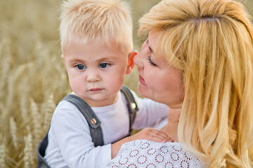 A beautiful blonde woman holds a blond son in her arms in a wheat field.