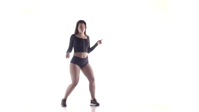 young sensual beautiful woman dancer with long hair in fishnet tights and shorts vigorously dancing dancehall twerk, street modern dance, long shot, isolated