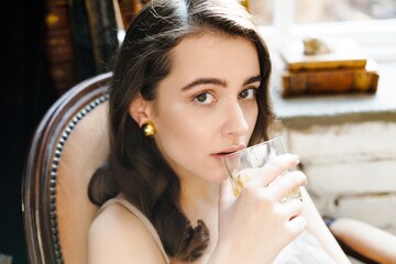 young attractive woman sitting in vintage armchair and holding glass of whiskey. Sensual woman with perfect skin and with natural makeup. fashion and style concept