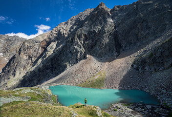 Naklejka na ściany i meble Man standing at turquoise lake Vordersee in Gradental national park Hohe Tauern with mountain in the background, Austria.