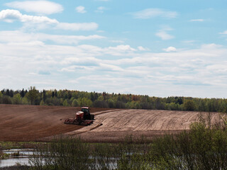 the tractor is sowing corn on the field. agriculture, farming. near the forest and the river