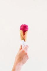 Raspberry ice cream cone on light brown background. Woman holding ice cream by hand. summer concept