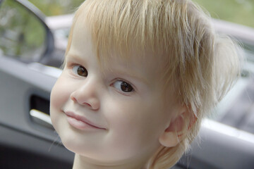 Close up of the face of a smiling little girl with blond hair in a car