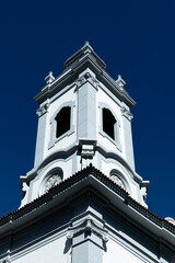 Bell tower with clocks brightly lit by noon sun part of the Saint Margarida Maria church in Rio de Janeiro near the city lake Lagoa Rodrigo de Freitas
