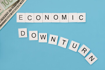 Phrase economic downturn spelled out in wooden letter tiles on trendy blue background. Economic and financial crisis concept. global economic recession. Top view. Flat lay