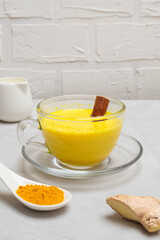 Cup of turmeric golden milk with milk cane, turmeric powder and ginger root on concrete table