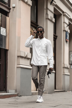 Young millennial african boy in city. Happy black man in jacket with camera. Generation Z concept.  Man walking on the street.Portrait of pensive modern afro man with sunglasses and camera