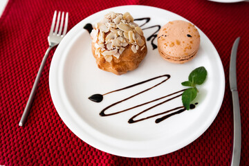 Homemade sweet profiteroles with custard, french biscuits macaroon and cup of coffee on red napkin . Spring or summer dessert concept. Close up. traditional french desserts