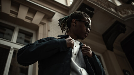 Young millennial african boy in city. Happy black man in jacket with camera. Generation Z concept.  Man walking on the street.Portrait of pensive modern afro man with sunglasses and camera
