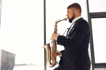 Fototapeta na wymiar Man in a studio. Guy in a black suit. Musician with saxophone.