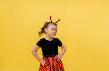 A dreamy little girl in a ladybug costume looks away on a yellow isolated background with space for text.