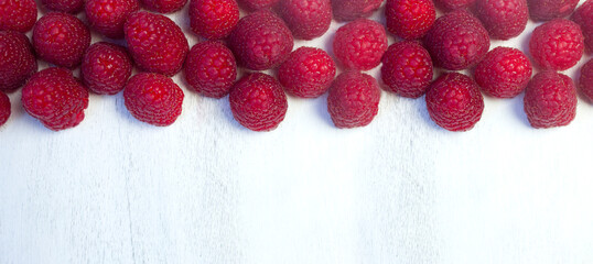 Red fresh raspberries on white rustic wood background, top view