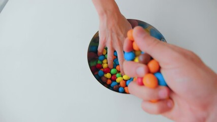 Two people take fistful of candy from bowl with colourful chocolate sweets on isolated white background. Friends enjoy sweet treats or snacks at party or halloween