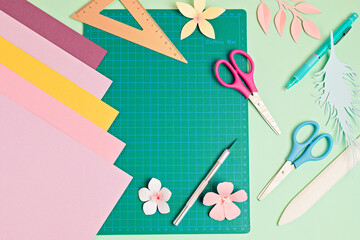 Top view over paper cut tools, scissors, cutter, cutting mat, and crafted paper objects. DIY trendy project concept