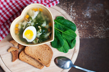 Green borsch with sorrel, parsley, egg and grens in the bowl form of heart with spoon on wooden background. Top view
