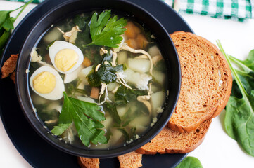Green borsch with sorrel, parsley, egg and grens in black bowl with spoon on white background. Top view