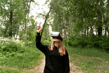 girl stands in the middle of the forest in virtual glasses is surprised stretches her hand to the top