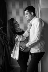 Romantic couple expecting baby, holding hands and touching foreheads while standing together against window at home, free space. Pregnancy, maternity, preparation and expectation concept. C