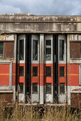An exterior view of the back exit doors of an old weathered street car in field of grass
