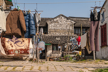 Tongli, JIangsu, China - May 3, 2010: Laundry dries along alley in poor gray-stone houses with dark roofs under blue sky. Weeds between stones add color.