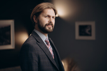 Portrait of confident mature man in business suit posing on camera with blur background of modern office. Concept of successful career, finance and people.