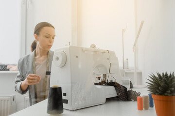 Picture of young woman tailor working on a sewing machine with sun reflection