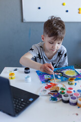 boy paints, online drawing classes, gray Tshirt with stars, laptop on the table