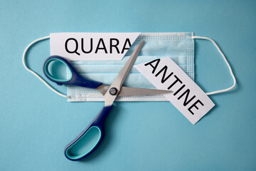 Scissors cutting a protective mask and piece of paper with quarantine word. Isolation is over. Back...