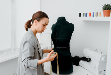 Young woman tailor is measuring with a centimeter ribbon the waist of a mannequin