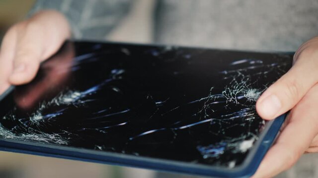 A man holds a tablet with a broken screen