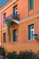 Fototapeta na wymiar Orange stucco building with deep green and white casement windows in Athens Greece with wrought iron balcony and succulent growing down almost to ground - Close-up