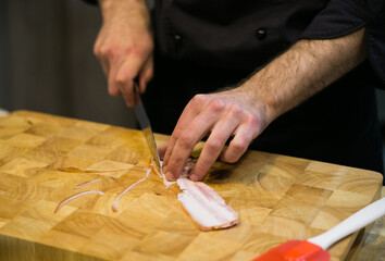 chef cuts bacon with a knife on a wooden cutting board