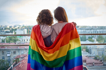 Two girls looking out the window at the city with rainbow flag