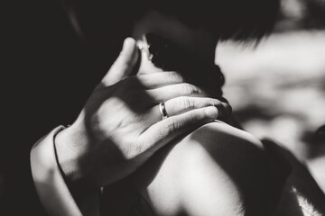 Black and white closeup photo of grooms hand laying on bride shoulder. Husband wearing wedding ring. wedding day concept.