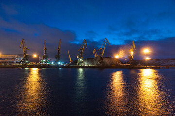 Fototapeta na wymiar Night view of the coal terminal of the cargo port. Cargo cranes await the arrival of the vessel for loading coal. The freight train awaits unloading of coal in the port